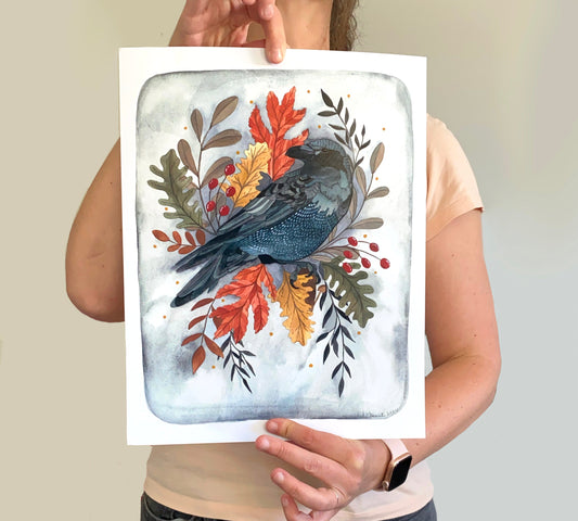 Person holding a painting of a bird surrounded by autumn leaves and foliage.