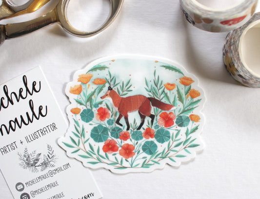 Sticker with a fox design and floral elements on a white surface with stationery items.