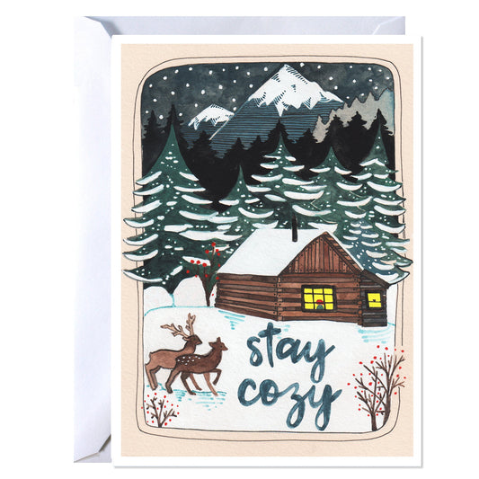 Greeting card with a winter scene featuring a cabin, trees, and deer, with 'stay cozy' text.