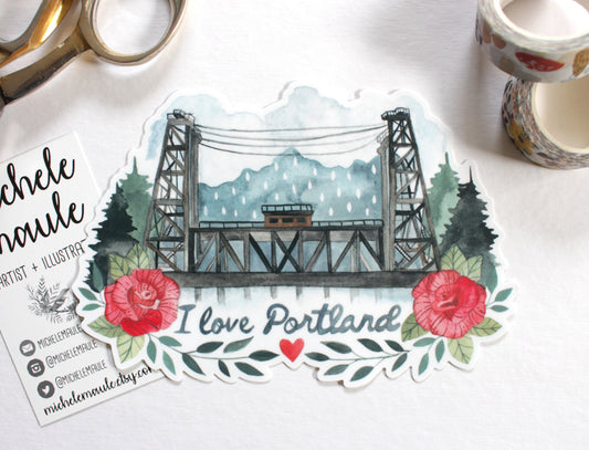Sticker with a bridge design and 'I love Portland' text, surrounded by stationery items.